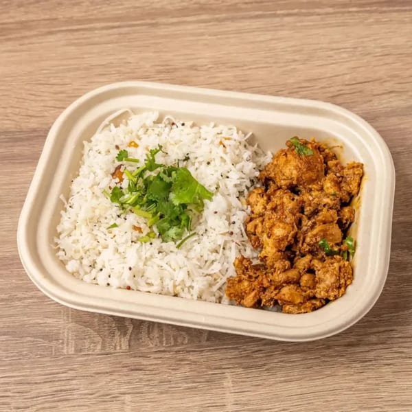Indian chicken curry and rice with cilantro in a takeout container on a wooden table.
