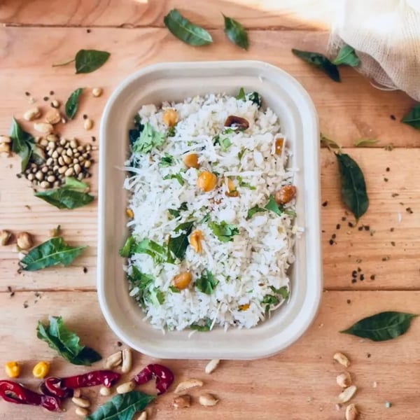 Kolapasi Indian Canteen's coconut rice with peanuts and herbs, surrounded by spices on a wooden table.