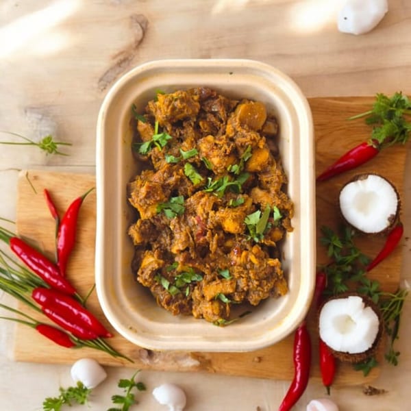 Kolapasi Indian Canteen's chicken curry in a to-go container, garnished with cilantro, chilies, and coconut.