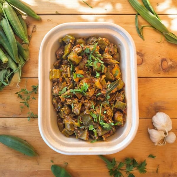 Kolapasi Indian Canteen's okra curry, garnished with cilantro, on a wooden table with fresh okra and garlic.