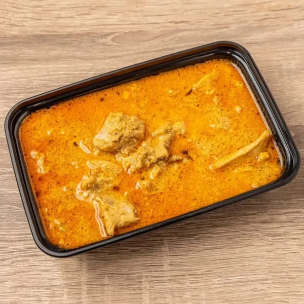 Indian chicken curry in a black rectangular takeout container on a wooden surface.