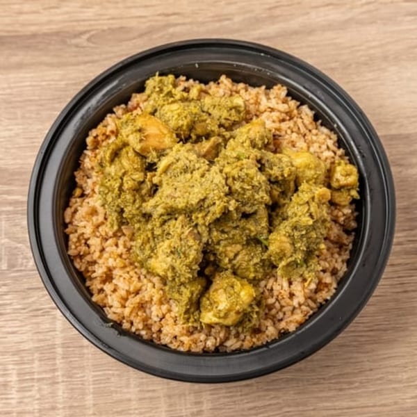 Kolapasi Indian Canteen's green chicken curry with rice in a black bowl on a wooden table.