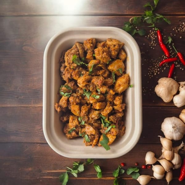 Indian chicken curry in a to-go container, garnished with cilantro, surrounded by spices.