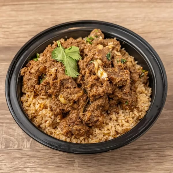 Indian lamb biryani with rice and cilantro in a black bowl on a wooden table.